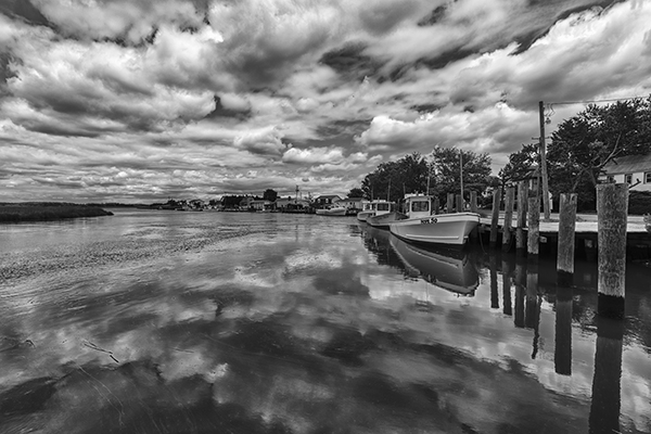 View from Sambo's Dock in Smyrna DE with fishing boats and dramatic sky and reflections in black and white